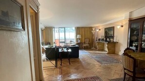 A spacious living room with a large rug, a dining area with a table and chairs, and a kitchen in the background. - Incantevole Attico in Via Del Corso (Roma)