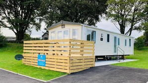 Een stacaravan met een 'Te Koop'-bord, een schotelantenne en een klein terras.