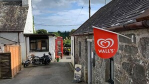 Een smalle straat met stenen gebouwen, een motorfiets geparkeerd ervoor, en een rood bord met de tekst WALL'S.