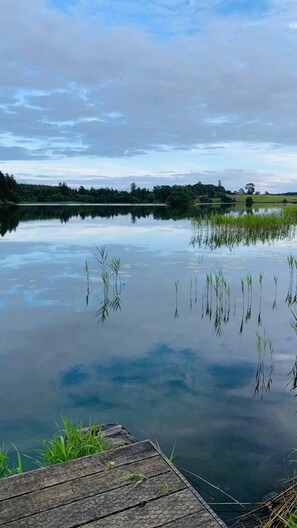 Um lago calmo com um píer de madeira que se estende sobre a água, rodeado por vegetação e árvores.