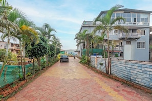 A residential street with a paved walkway, palm trees, and houses with balconies. - Treebo Kuber Palace With a Swimming Pool (Mahabaleshwar)