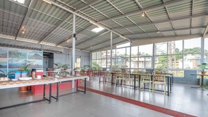 A spacious indoor area with a high ceiling, large windows, and a long counter with chairs. - Treebo Kuber Palace With a Swimming Pool (Mahabaleshwar)