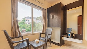 A room with a window, two chairs, a table, a mirror, and a shelf with items. - Treebo Kuber Palace With a Swimming Pool (Mahabaleshwar)