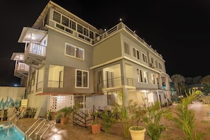 A two-story building with a swimming pool, potted plants, and a staircase leading to the entrance.