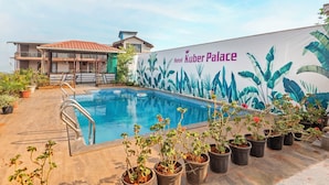 A swimming pool with potted plants, a building with a balcony, and a mural of tropical leaves. - Treebo Kuber Palace With a Swimming Pool (Mahabaleshwar)