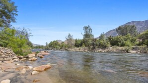 A river with clear water, surrounded by rocks and greenery, with mountains in the background.