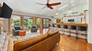A spacious living area with a large brown sofa, a green armchair, and a wooden dining bar with bar stools.