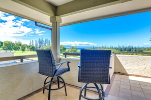 A balcony with two wicker chairs, a view of a golf course, and a clear blue sky.