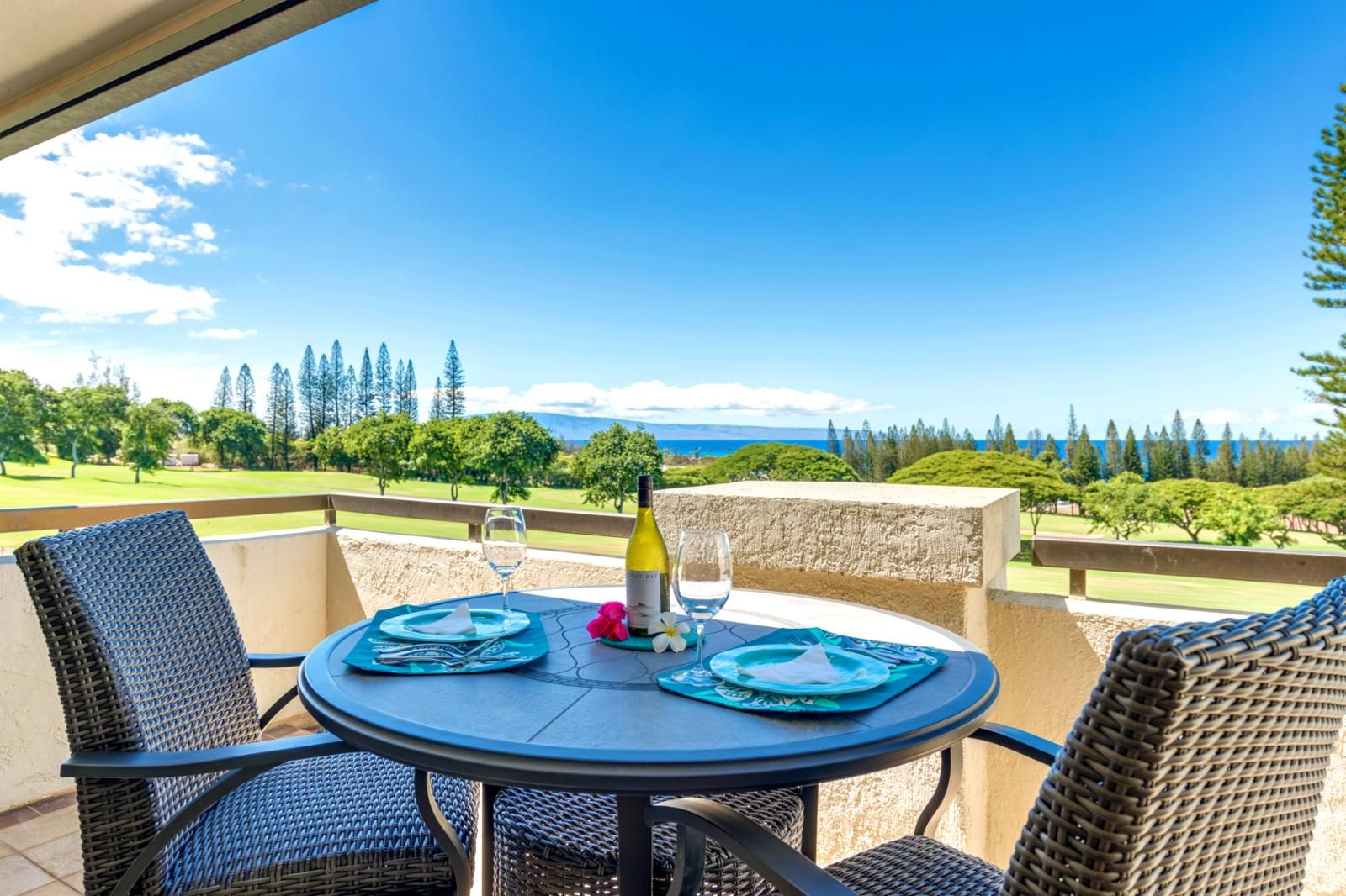 Ein runder Tisch mit zwei Stühlen auf einem Balkon mit Blick auf einen Golfplatz und den Ozean.