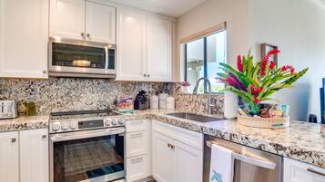 A kitchen with white cabinets, a granite countertop, stainless steel appliances, and a window with a view.