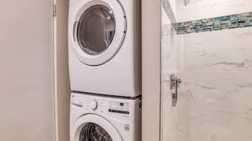 A stacked washer and dryer unit in a bathroom with a tiled backsplash.