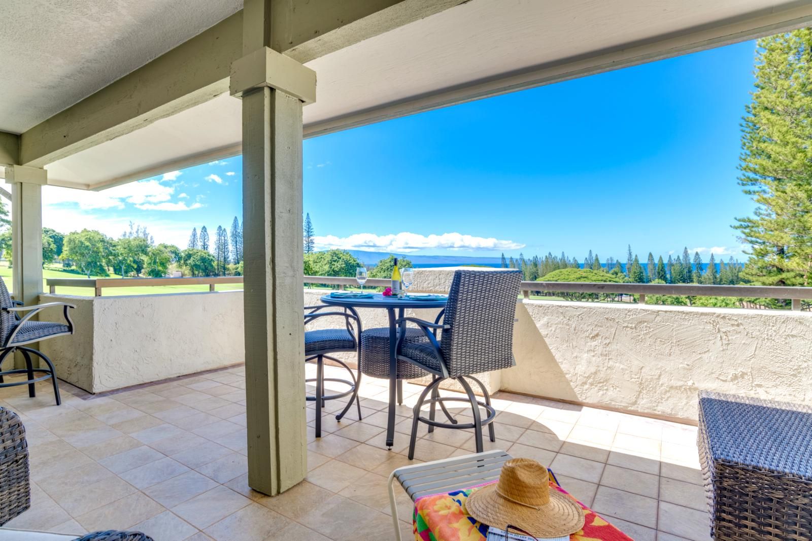 A covered patio with a table and chairs, overlooking a scenic landscape with trees and a view of the ocean.