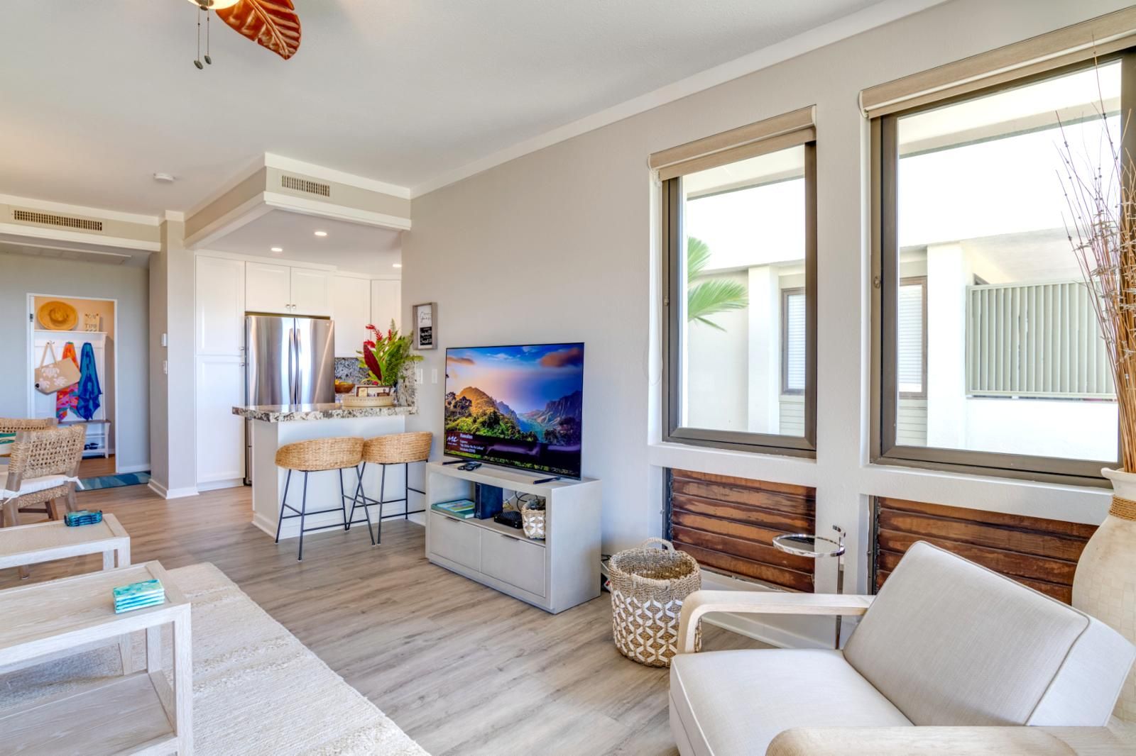 A modern living room with a TV, seating area, and a kitchen in the background.