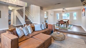 A spacious living room with a brown leather sectional sofa, a woven ottoman, and a dining area with a table and chairs.