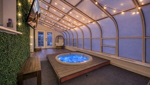 A hot tub in a room with a curved ceiling, a chair, and a television on a shelf.