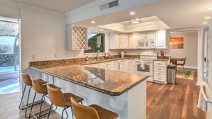 A modern kitchen with a large island, bar stools, white cabinetry, and a view of the outdoors.