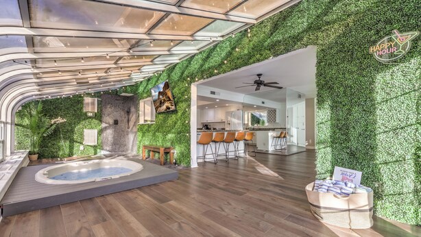 A modern interior with a hot tub, wooden flooring, green wall, and a kitchen area.