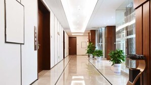 A modern hotel corridor with a polished floor, wooden lockers, and potted plants. - Donghu Hotel (Yichun)