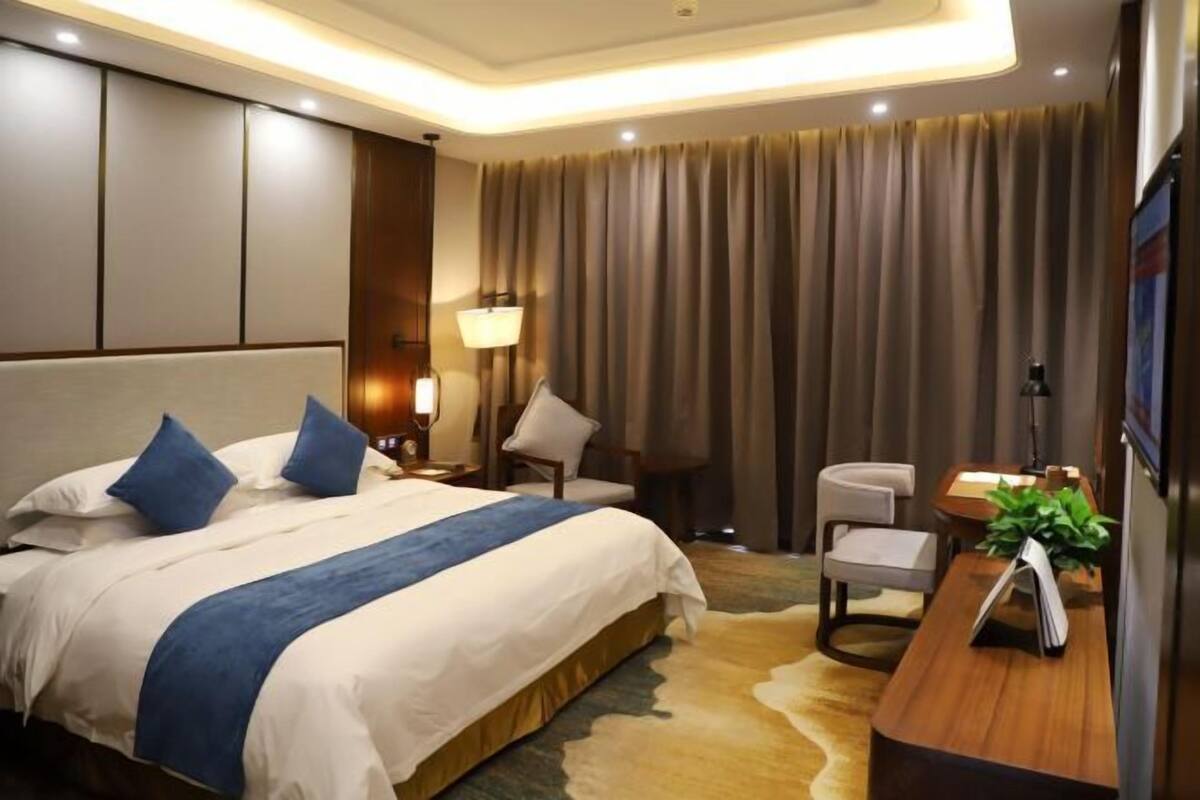 A hotel room with a large bed, a desk, a chair, a lamp, and a television.