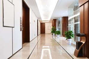 A hotel corridor with a polished floor, wooden doors, and potted plants.