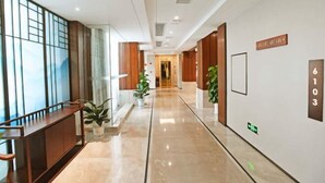 A modern hotel corridor with a polished floor, wooden paneling on the walls, and potted plants. - Donghu Hotel (Yichun)