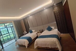 A hotel room with two beds, a large window, and a view of greenery.