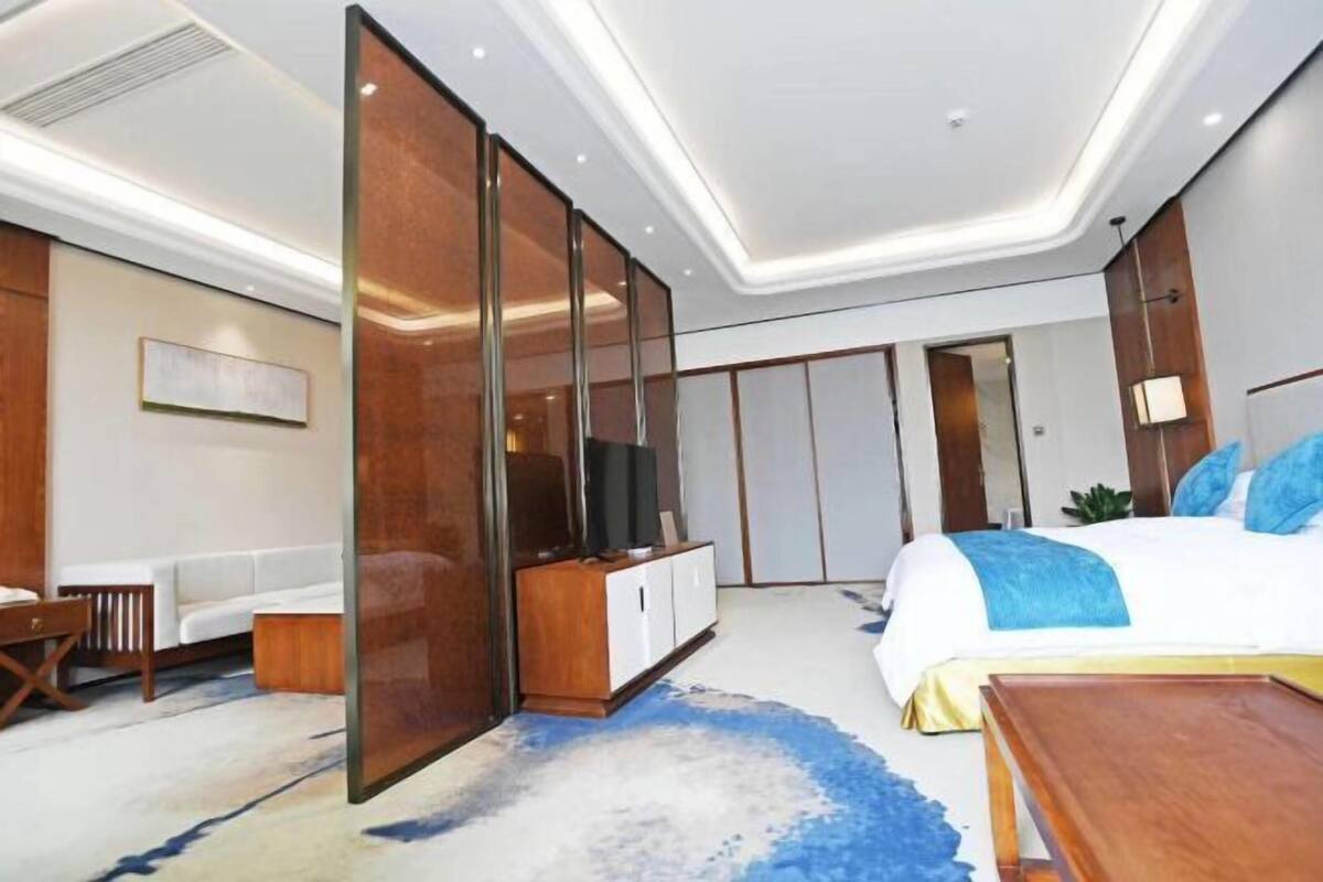A modern hotel room with a bed, a TV, a sofa, and a wardrobe.