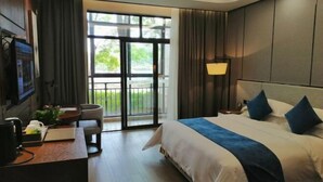 A hotel room with a large bed, a desk with a computer, a chair, and a view of the outdoors through a sliding door. - Donghu Hotel (Yichun)