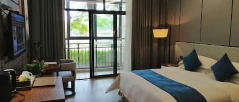 A hotel room with a large bed, a desk with a computer, a chair, and a view of the outdoors through a sliding door.