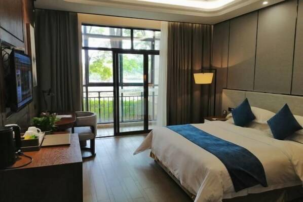 A hotel room with a large bed, a desk with a computer, a chair, and a view of the outdoors through a sliding door.