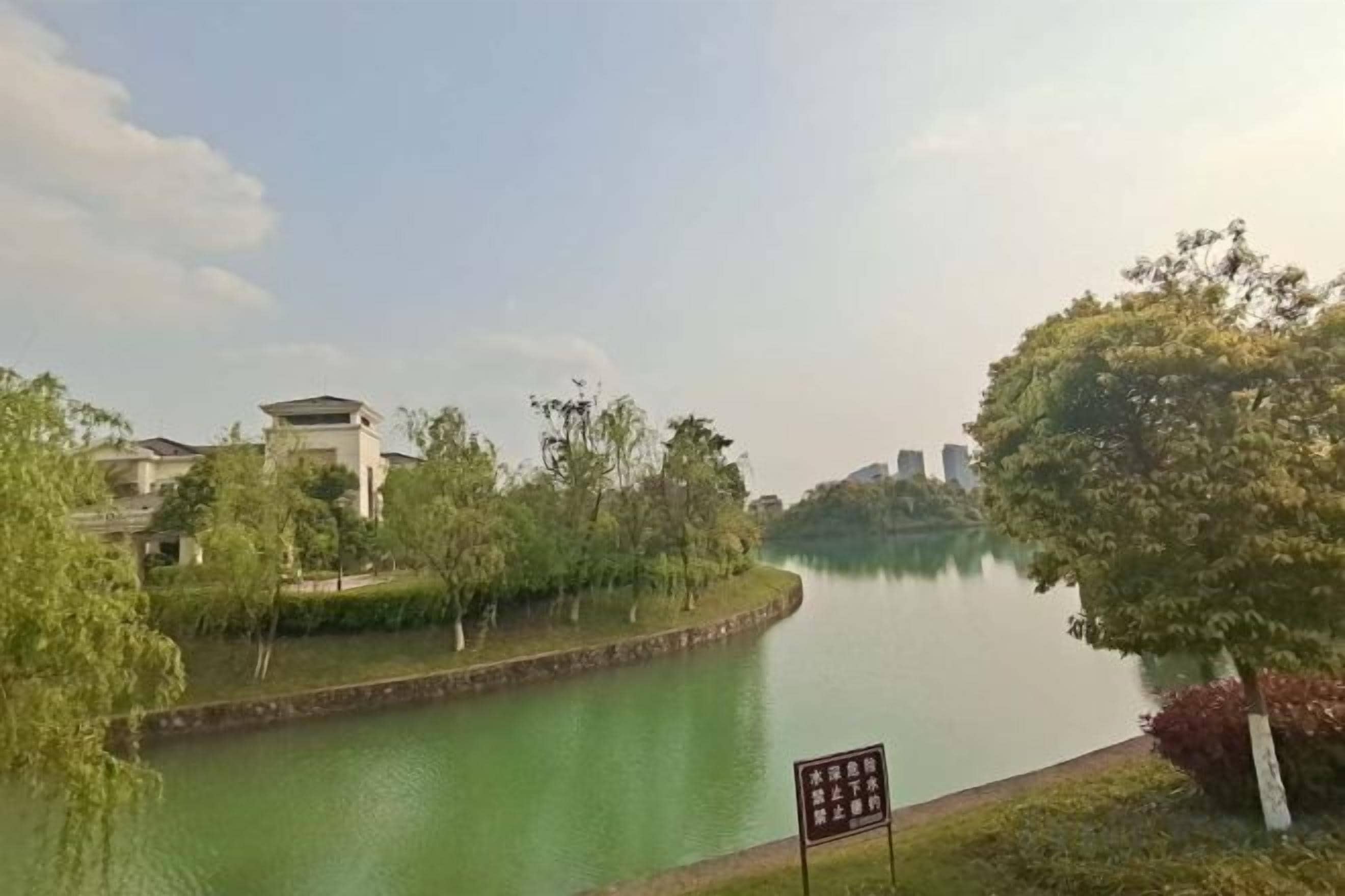 Un río tranquilo con un puente, rodeado de vegetación y edificios.