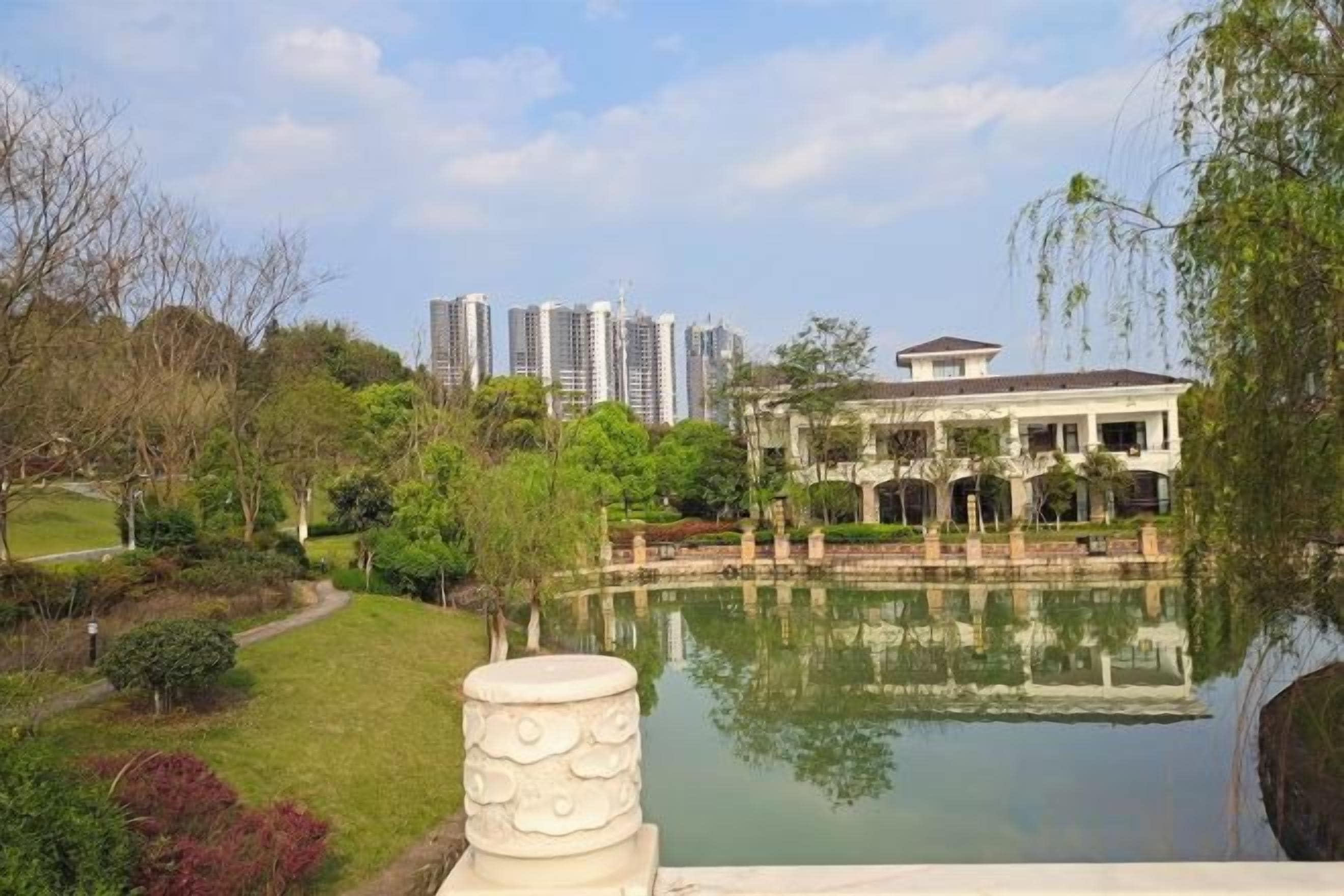 Un parc paisible avec un étang, un bâtiment dont le reflet se mire dans l’eau, et des immeubles de grande hauteur en arrière-plan.