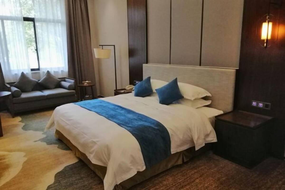 A hotel room with a large bed, a sofa, a nightstand, and a lamp.