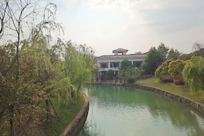A building with a pond in front, surrounded by trees and greenery.