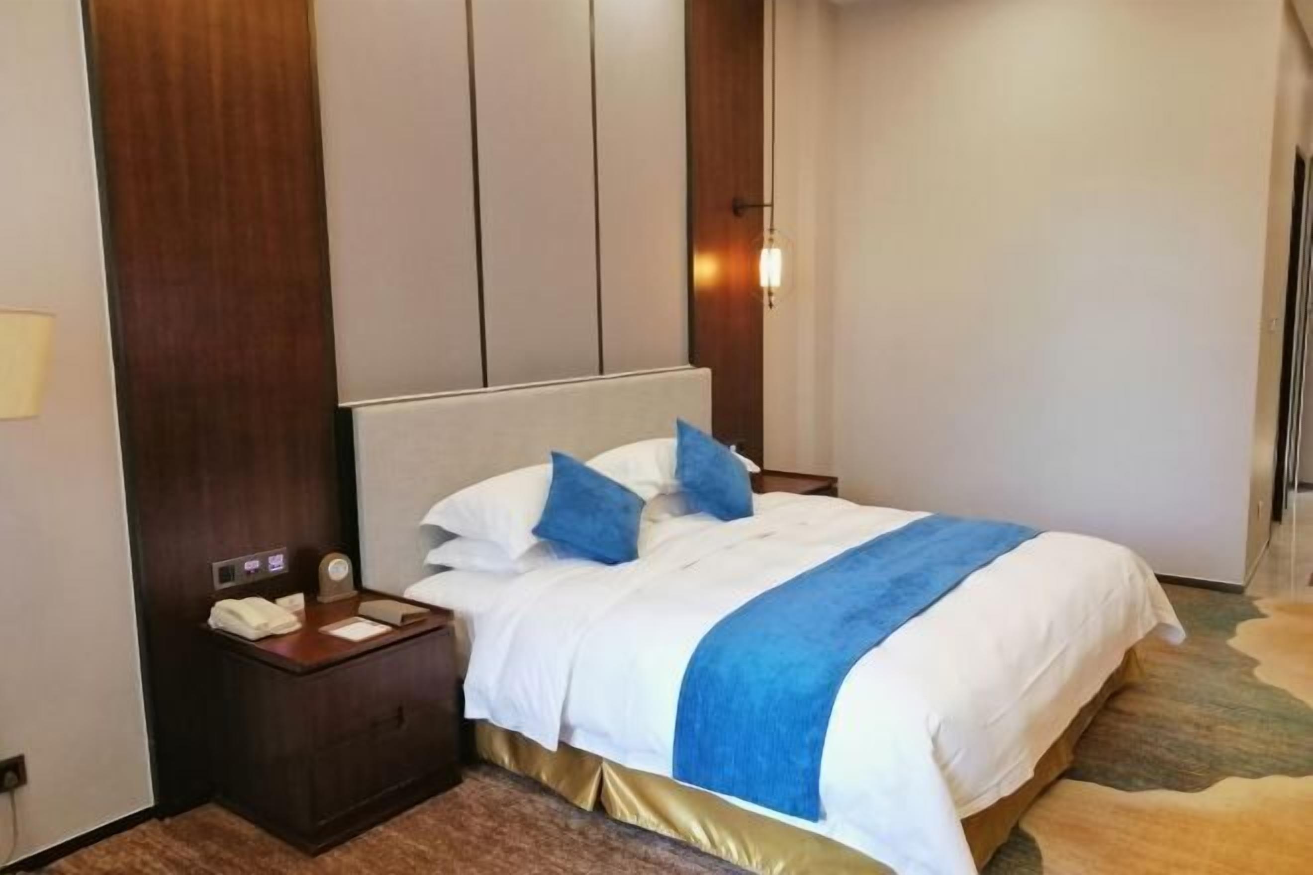 Habitación de hotel con una cama grande, una mesita de noche de madera, un escritorio y una lámpara fijada a la pared.