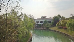 A serene riverside view with a building featuring a central pavilion and a stone pathway leading to it. - Donghu Hotel (Yichun)