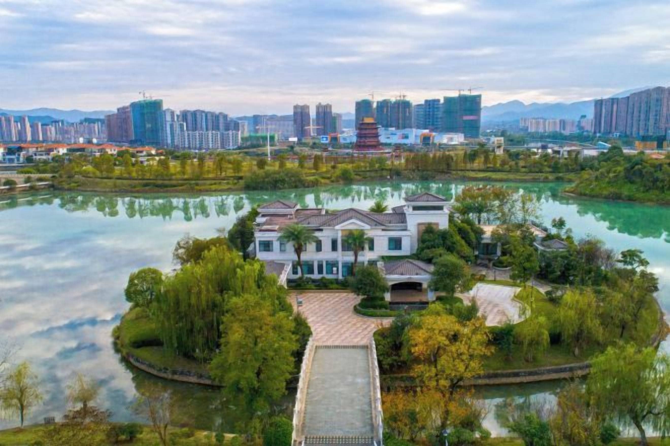 Una propiedad a orillas del río con un puente, una casa grande y un paisaje urbano al fondo.