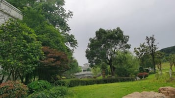 A lush garden with a variety of trees and shrubs, a stone bridge, and a large rock in the foreground.
