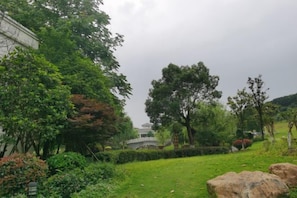 A lush garden with a variety of trees and shrubs, a stone bridge, and a large rock in the foreground. - Donghu Hotel (Yichun)