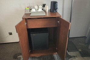 A compact wooden desk with a small refrigerator, a coffee maker, and a tray with cups and a teapot.