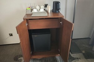 Un escritorio de madera compacto con un pequeño refrigerador, una cafetera y una bandeja con tazas y una tetera.