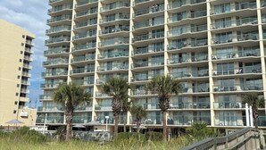 A high-rise building with multiple balconies, a wooden boardwalk, and palm trees. - Ashworth 1001 4-Bedroom Oceanfront Condo, "Picture Perfect" (North Myrtle Beach)