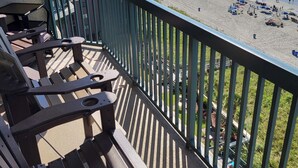 A balcony with wooden chairs and a view of a beach with umbrellas and people. - Ashworth 1001 4-Bedroom Oceanfront Condo, "Picture Perfect" (North Myrtle Beach)