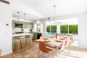 A modern kitchen with a dining area, large windows, and a view of a swimming pool.