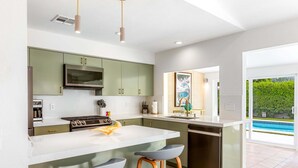 Una cocina moderna con una isla central, electrodomésticos de acero inoxidable y vistas a una piscina.