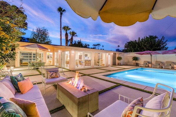 A poolside area with a fire pit, lounge chairs, and a covered seating area.