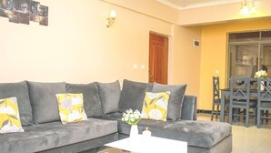 A living room with a grey sofa set, a coffee table, and a dining area with a table and chairs. - Impeccable Family Friendly Apartment in Nairobi (Nairobi)