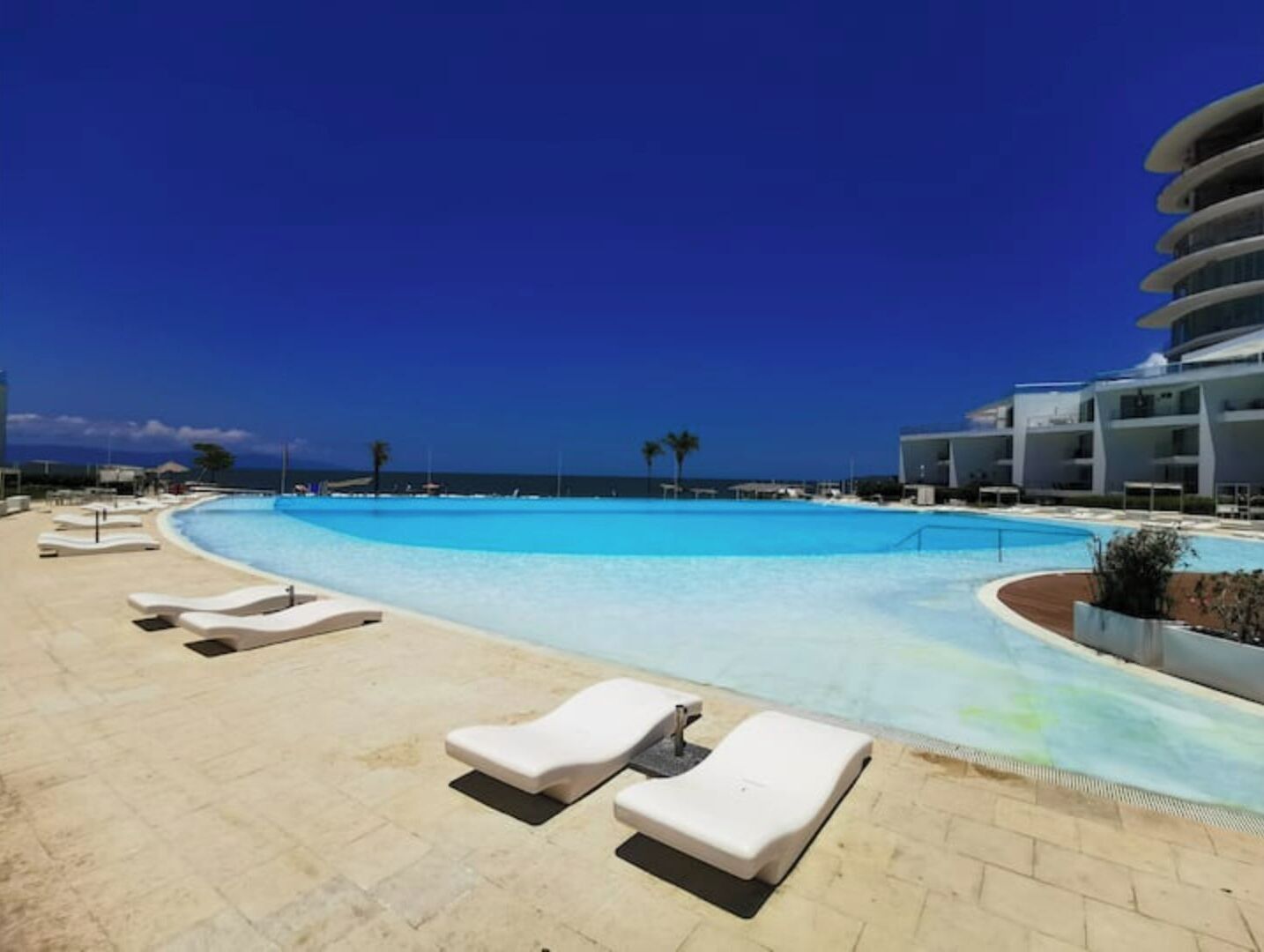 Un espace piscine avec des chaises longues, un ciel d’un bleu éclatant et une vue sur l’océan.