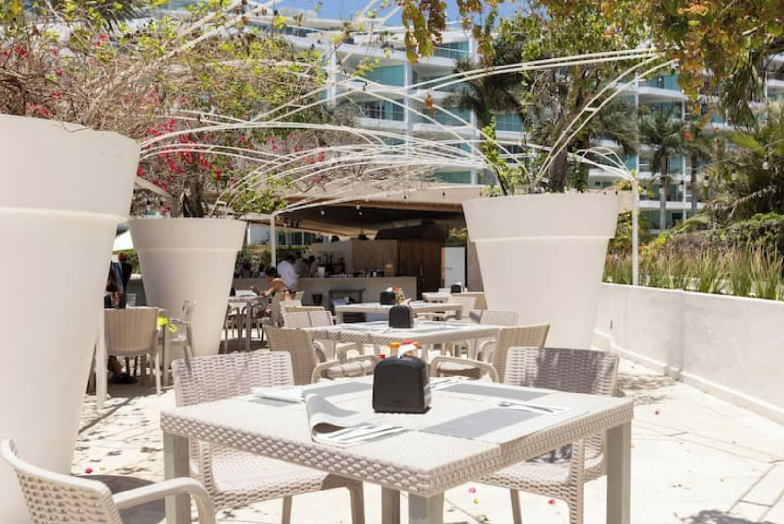 An outdoor patio area with white wicker furniture, a covered seating area, and a view of a modern building in the background.