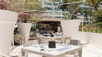 An outdoor patio area with white wicker furniture, a covered seating area, and a view of a modern building in the background.